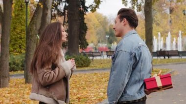 Genç erkek arkadaş küçük kırmızı kutuyu saklar gizli bir hediye verir. Sevgi dolu sevgililer gününü kutlayan güzel kıza sürpriz yapar. Parkta kucaklaşan sevimli çift.