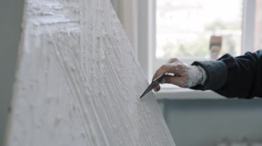 Tanımlanamayan kadın yaratıcı kadın kadın eller kadın ressam tasarımcı bilinmeyen kız macun bıçağı tutuyor pürüzsüz arka plan mala ekipmanlarıyla yapışkan beyaz yapışkan dokuyu tuvale yayıyor