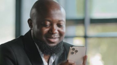 Afrikalı erkek kullanıcı patronu işverenin elinde modern cep telefonu tomarı web sayfaları var. Sosyal ağlarda kurumsal video sohbetlerini izliyorlar. Ofis wifi okuma sohbetlerini kullanarak medya haberlerine mesajlar yolluyorlar.