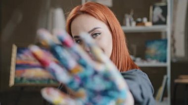 Kafkasyalı kızıl saçlı kadın ressam kız, resim stüdyosunda resim yaptıktan sonra resim stüdyosunda değil, kolunun önünde el ele tutuşarak renkli avuç içi boyalarıyla resim yapıyor.
