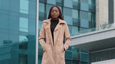 Genç, ciddi, kendine güvenen başarılı iş kadını arka plandaki ofis binasının önünde duruyor şık, Afro-Amerikan kadın model sonbahar montu giymiş kameraya bakıyor.