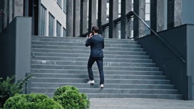 Resmi takım elbiseli başarılı bir işadamı merdivenlerden çıkıp modern ofis binasına çıkıyor profesyonel erkek satış temsilcisi telefonda müşteriyle iletişim kuruyor.