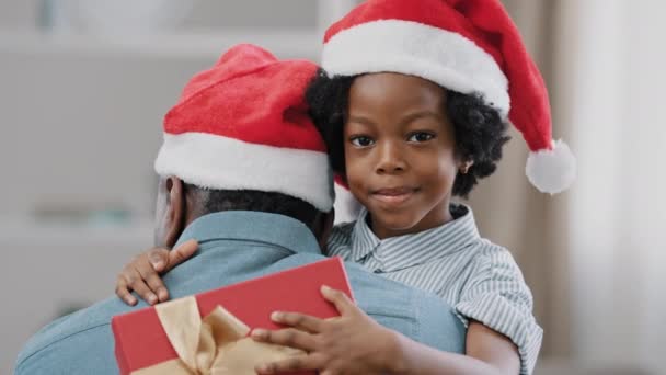 クローズアップ幸せなかわいい子供の女の子は持っているカメラを見てサンタ帽子抱擁お父さんを身に着けています新年のボックスお祝いクリスマス家族のかわいい愛情のある娘喜びで休日を楽しんでギフト抱擁お父さん — ストック動画
