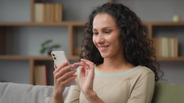 在家里惊讶的女人脸上的惊讶的白种人西班牙裔拉美裔30多岁的女人用手机聊天 用手机打赌应用程序读到了好消息 笑着对着相机看 — 图库视频影像