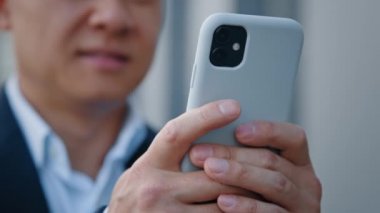 Bulanık Asyalı orta yaşlı bir adamın cep telefonuyla konuşan, internette mesajlaşan, internette gezen, mobil uygulamalarla çalışan açık havada rezervasyon yaptırmak için telefon kullanan erkek ellerini kapat.