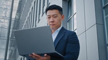 Asyalı, orta yaşlı, yetişkin, 40 'lı yaşlarda bir iş adamı mimar şehir merkezindeki açık havada dizüstü bilgisayarı daktilo ederek internetteki proje uygulaması tarayıcısıyla çalışıyor.