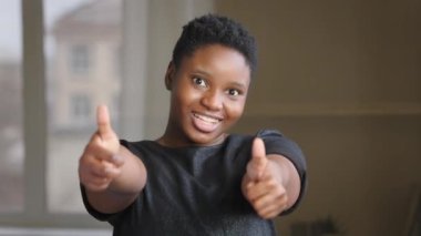 Melez, mutlu, kısa saçlı, neşeli, gülümseyen Afrikalı Amerikalı bir kadın. Kameraya bakıyor, destekliyor. Harika bir jest.