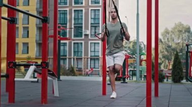 Kas sporcusu Afrikalı sporcu spor giyim sporunda formda bacak egzersizi yapıyor. Ağırlık TRX kayışları kullanarak spor sahasında çömelme egzersizi yapıyor. Yüksek diz direnci eğitimini kaldırıyor.