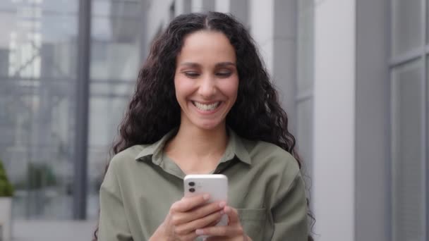 ヒスパニックラテン白人30代の女性ユーザーブロガー女性屋外で携帯電話を使用して都市のブラウジング受信オファースマートフォンの波の頭の上に指でSmsポイントはいオンラインアプリをお勧めします良い接続 — ストック動画