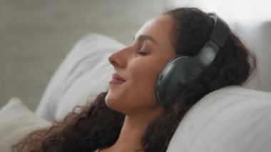 Yakın çekim mutlu sükunet İspanyol asıllı beyaz kadına ilham verdi. Kanepeye uzanmış, gözleri kapalı, kablosuz kulaklıkla müzik dinleyen bir kadın. İnternetteki şarkı sesi evde bozuldu.