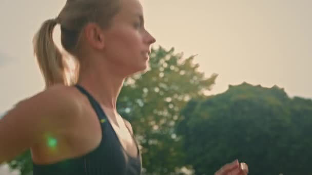 黒のスポーツウェアジョギング強烈なスプリントのアスリートの女の子は朝日が昇る朝の光線の中で屋外ワークアウトを実行している レースやマラソンのためのカーディオを練習ブロンドのスポーツウーマンランナーの側面図 — ストック動画