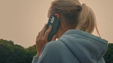 Sarışın, sportif bir kadının arkasına dönüp baktığımızda cep telefonuyla konuşan, cep telefonuyla konuşan genç bir kadının modern akıllı telefonu kullanarak iletişim kurduğu kablosuz bağlantı kurduğunu görüyoruz.