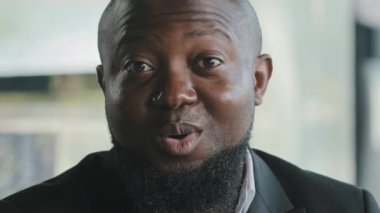 Olumlu, neşeli, yetişkin, erkek, işadamı Afrikalı, Amerikalı, esmer, sakallı, memnun müşteri, ofiste zafere seviniyor.