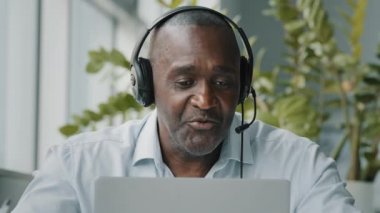Kıdemli Afrikalı çalışan, ofis masasında oturup mikrofonlu kulaklık takıyor. İnternetteki internet sohbetinde web kamerasıyla iletişim kuran iş görüşmesine mikrofon bağlanıyor.