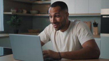 Aşırı sevinçli Afrikalı Latin erkek adam evinde mutfakta online bahis oynuyor. Dizüstü bilgisayarlı bahsi kazan. İnanılmaz iyi haber duygusal kutlama teklifiyle heyecan verici.