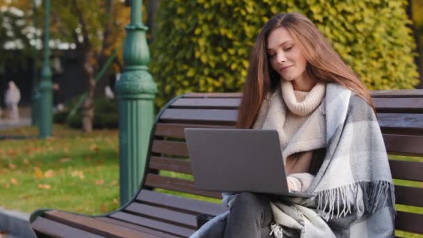 白人の若い女性実業家の学生は 遠隔通信のためのコンピュータウェブカメラを使用して交渉ノートパソコンのビデオ通話会議でオンラインで公園のチャットでベンチに座っています流行のフリーランスの仕事屋外 — ストック動画