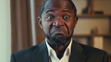 Kafası karışmış yetişkin Afro-Amerikan işadamı omuz silkiyor. Cevap vermiyor. Kafası karışmış adam kameraya bakıyor.