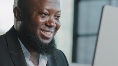 Gülümseyen Afrikalı iş adamı yetişkin profesyonel çalışan web tasarımcısı internette sohbet ediyor ofisteki kablosuz interneti kullanarak bilgisayardaki dijital bilgileri araştırıyor internetten iş sitelerini izliyor.