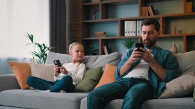 Odaklanmış baba ve kız çocuk kanepeye oturur akıllı telefon cihazları kullanır telefon ekranlarında sohbet eder mobil uygulamalar yükler çeşitli nesiller çeşitli aletlerden bağımlıdır modern teknoloji aşırı kullanımı