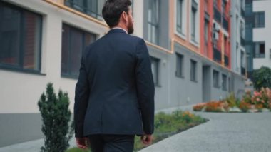 Takım elbiseli, kendine güveni tam bir adam şehir sokaklarında başarılı bir işadamı olarak iş yerine gidiyor manzarası olan bir yerleşim bölgesinde yürüyor modern şehir mimarisinin yeni konutlarının keyfini çıkarıyor.