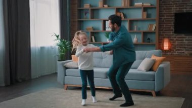 Mutlu milenyum babaları, güzel sanatsal kızlarıyla dans ederek çocuk dansı öğretir. Aktif anaokulu çocuğu, babasının elini tutar. Oturma odasında eğlenceli bir ev partisinde birlikte müzik eşliğinde zıplar.