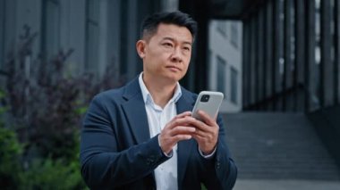 Şehirdeki orta yaşlı Asyalı işadamı, 40 'lı yılların lider şirket CEO' su, girişimci açık havada, telefon düşünerek sorunların çözümünü arıyor. Akıllı telefondan yaratıcı bir karar vermeyi düşünün.