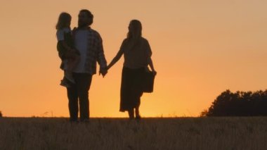 Aile babası, anne ve kız üç kişinin siluetleri. Anne ve kız çocuğu akşamları buğday tarlasında yürüyorlar. Gün batımında güneş ışınları doğada yaz güneşinin doğuşunda birlikte gidiyorlar.