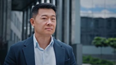 Düşünceli, düşünceli bir işveren, hayal kurarken kameraya dönüp, Asyalı, Koreli, iş adamı, patron, şirket CEO 'su, ofis binası yakınında mutlu, orta yaşlı bir işadamı gülümsüyor.