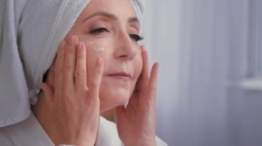 Yaşlı olgun beyaz kadın masaj yapan buruşuk suratlı kadın. Kırışıklık önleyici cilt kremi sürüyor. Kapalı cilt kremi.