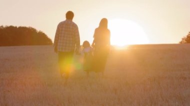 Aile silueti, anne-baba-kız, baba-kız çocuk yürürken sarı altın tarlada yürürken gün batımında gün batımında parkta güneş ışığı.