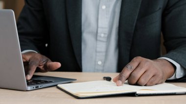 Close-up male hands writing in notebook with pen make notes information financial analysis startup project management idea sitting at desk in office using laptop unrecognizable middle-aged businessman