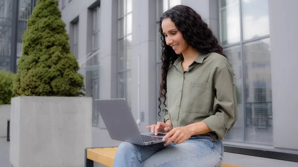 ヒスパニック系の女性ビジネスレディー30ビジネス女性フリーランスは 市内でラップトップ作業と屋外の束に座っているオンラインチャットネットウェブサイトサービスを使用してマーケティングプロジェクトを管理コンピュータを入力 — ストック写真