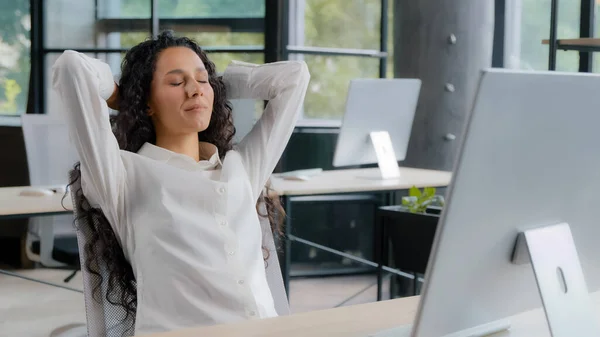 Young attractive hispanic woman office manager businesswoman typing on computer carefree female professional worker finishes work leans back on back chair puts hands behind head relaxing enjoying rest