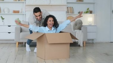 Hispanik adam şefkatli koca sevgili sevgili sevgili karton kutu itiyor sevgili karısı kıvırcık saçlı güzel kadın pakette oturuyor, taşınmayı kutluyor yeni bir ev satın alıyor.