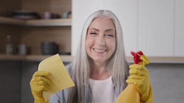 Mutlu kadın temiz işçi, yaşlı beyaz kadın kameraya poz veriyor sarı lastik eldivenler, temiz sıvı dezenfektanla bez ve sprey şişeyi tutuyor ve mutfak temizliğine hazırlanıyor.