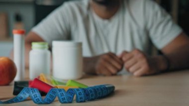 Yakın plan tanınmayan erkek beslenme uzmanı, elma ve vitamin haplarıyla masada oturuyor. İlaçlar ve mezura, video konferansında spor fitness diyet kalorileri hakkında konuşuyor. Sağlıklı beslenme