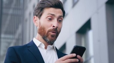Yakın plan neşeli adam elinde telefonla e-posta alıyor inanılmaz haberler okuyor hevesli iş adamı şaşırdı ve kazandı.