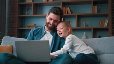 Baba ve küçük güzel kız çocuk dizüstü bilgisayarda video izliyorlar. Güzel beyaz aile gülüşleri. Hafta sonları evde dinlenin.