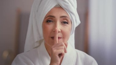 Kafkasyalı orta yaşlı, olgun, yaşlı, bornozlu, kafasında havluyla yaşlı bir kadın. Kameraya bakıyor. Sessizlik jesti yapıyor.