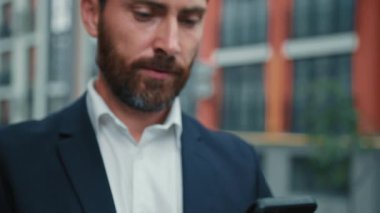 Başarılı yetişkin beyaz iş adamlarından esinlenerek şehirde sakallı zengin bir adam duruyor. Akıllı telefon kullan. Açık telefon kullan.