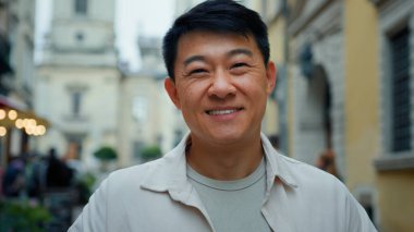 Kameraya bakıp gülümseyen dost canlısı bir erkek turist yeni şehirleri ziyaret ediyor tatilin keyfini çıkarıyor mutlu bir müşteri hafta sonu tatili tatilinin tadını çıkarıyor Asya modelinin yakın plan pozlarını veriyor.