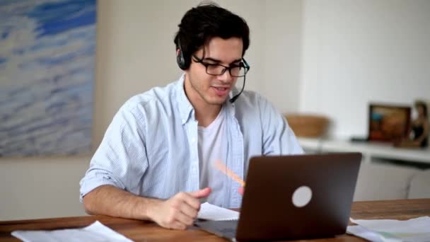 Feliz joven hispano seguro de éxito en auriculares, empleado del centro de llamadas o freelancer, trabajando remotamente en la computadora portátil, comunicándose a través de la comunicación por video con los empleados o el cliente, sonriendo — Vídeos de Stock