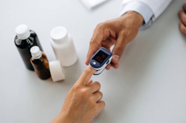 Oksijen doygunluğunu ve nabzı ölçmek için bir cihaz. Doktor hastaların oksijen doygunluğunu ve nabzını ölçmek için parmağına bir nabız oksimetresi takıyor. Üst görünüm