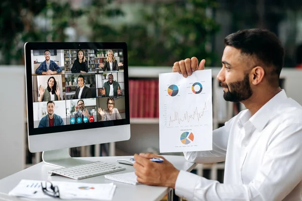 Vidéo conférence, réunion en ligne. Homme d'affaires indien intelligent ou mentor assis sur le lieu de travail, communique par appel vidéo avec ses partenaires, discuter d'une stratégie, montre un graphique financier — Photo