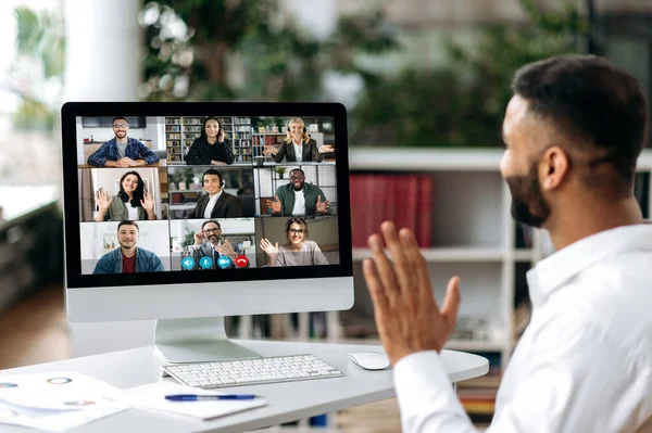 Video call, online conference. Over shoulder view of Indian man, on computer screen, talks with multinational group of successful business people, virtual business meeting, telecommunication concept — Stock Photo, Image