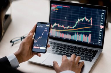 Dizüstü bilgisayarın ve diyagramlı cep telefonu ekranının yakın çekimi. Kripto borsa analizi, kripto para birimi alımı veya satışı için akıllı telefon ve dizüstü bilgisayar kullanan bir borsacı.