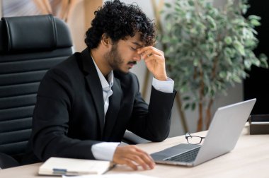 Hüsrana uğramış yorgun Hintli işadamı, menajer ya da bilişim uzmanı, ofiste bir masada oturuyor, gözlerine masaj yapıyor, dinlenmeye ihtiyacı var, stresli bir durum, baş ağrısı, migren.