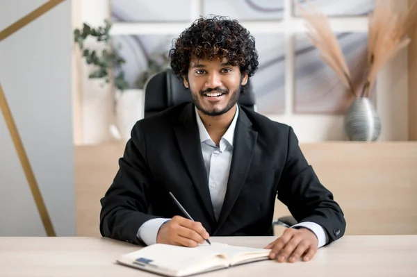 Amigável positivo bem sucedido indiana pessoa de negócios, mentor ou estudante, falando com colega ou cliente em conferência chamada, ter entrevista on-line, olha para a câmera, toma notas, sorrisos. E-learning — Fotografia de Stock