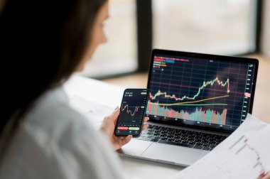 Dişi kripto tüccarı, yatırımcı, dizüstü bilgisayar ve cep telefonu kullanıyor, dijital kripto döviz borsası borsa grafiklerini analiz ediyor, analiz yapıyor, kripto piyasasının geleceğini düşünüyor.