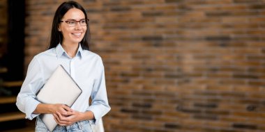 Kendine güvenen başarılı, zeki, beyaz bir kadın. Kadın ofis müdürü, öğretmen, mali danışman, ofiste duruyor, dizüstü bilgisayarı elinde tutuyor, yüzünü çevirmiş, arkadaşça gülümsüyor. Boşluğu kopyala, boş duvar